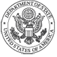 United States Department of State official seal. At the center of the round emblem, a bald eagle with wings spread holds arrows in one claw and an olive branch in the other.